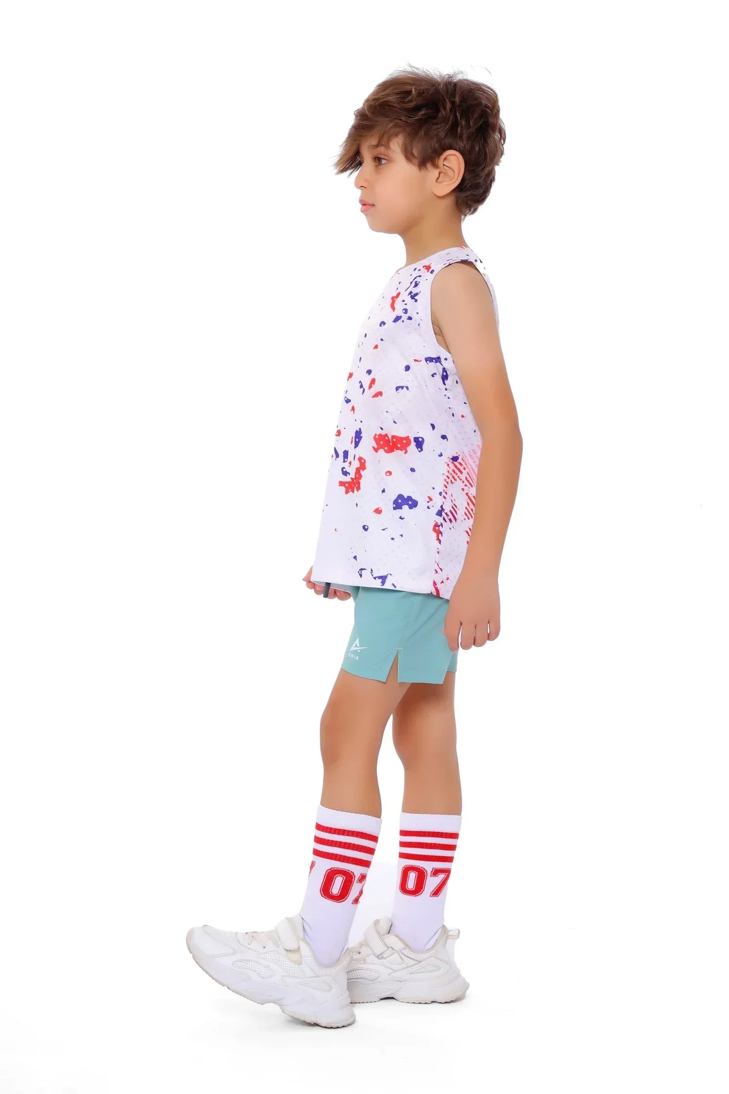 Child wearing a sleeveless shirt with colorful patterns, light blue shorts, and white sneakers on a white background