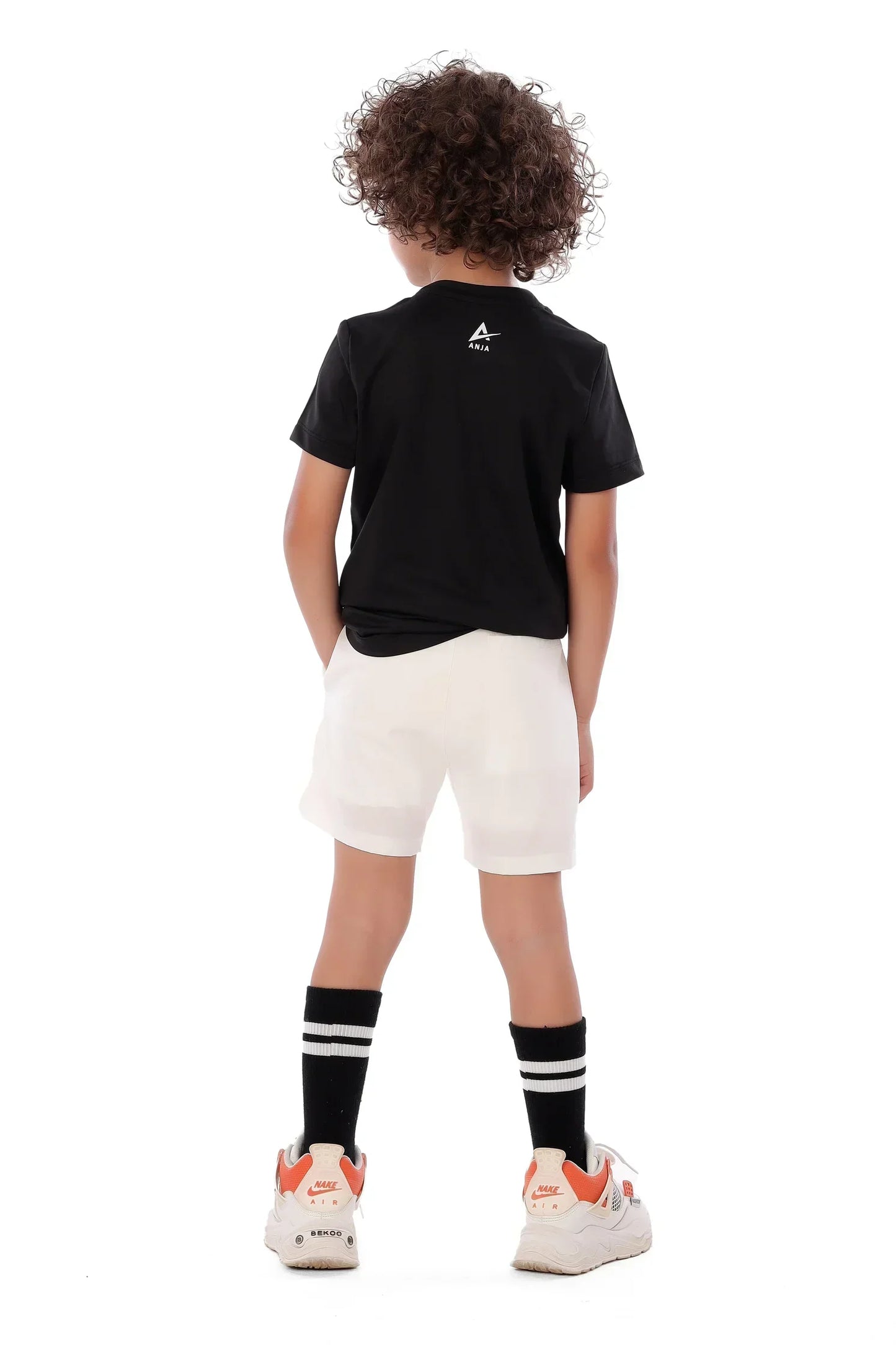 Child wearing a black t-shirt with a logo, white shorts, and black socks on a white background