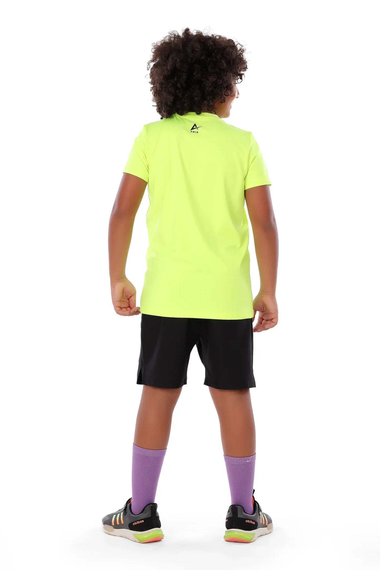 Child wearing a bright yellow sports jersey and black shorts on a white background