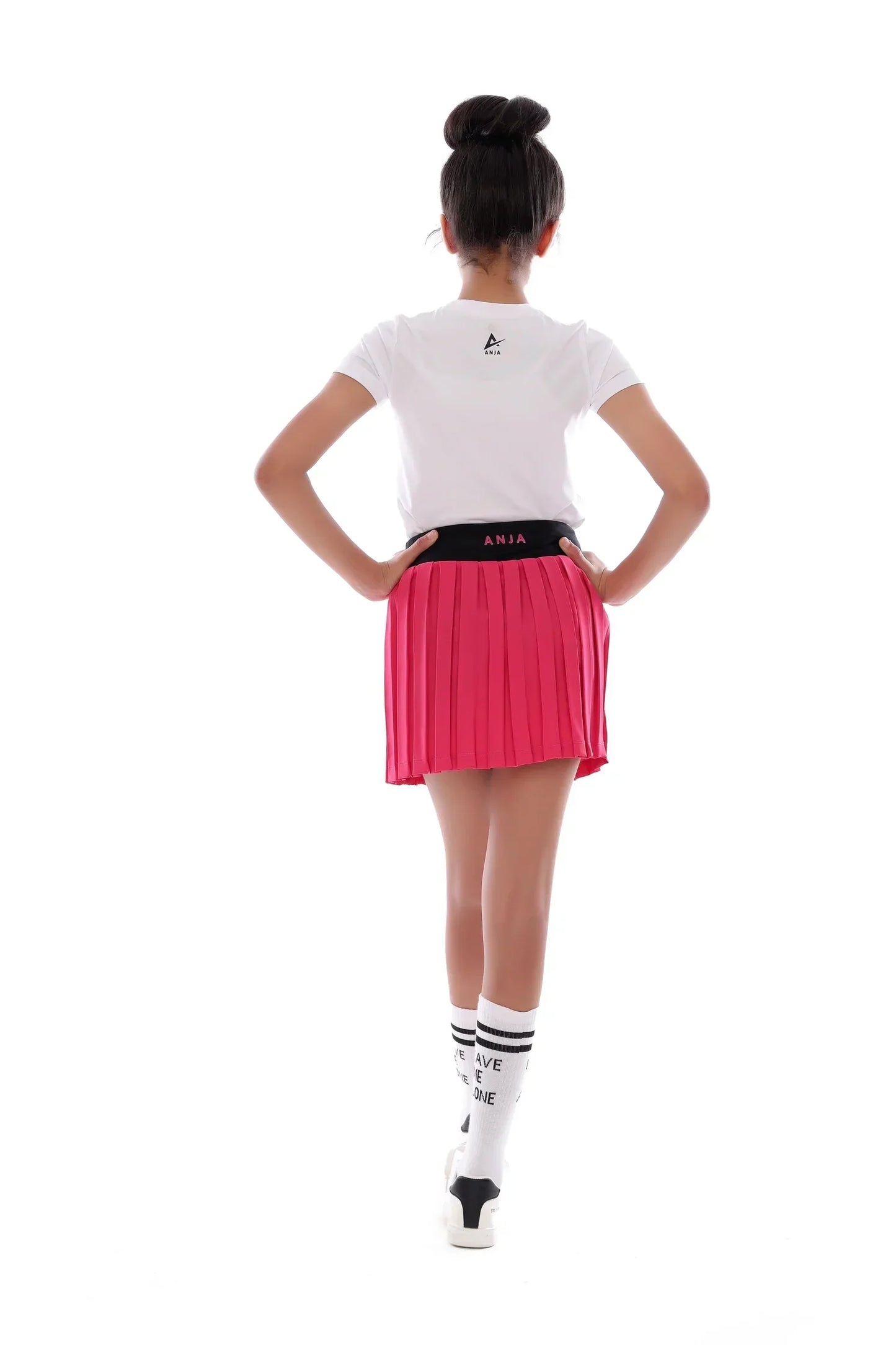 Person wearing a white t-shirt, pink pleated skirt, and black and white socks on a white background