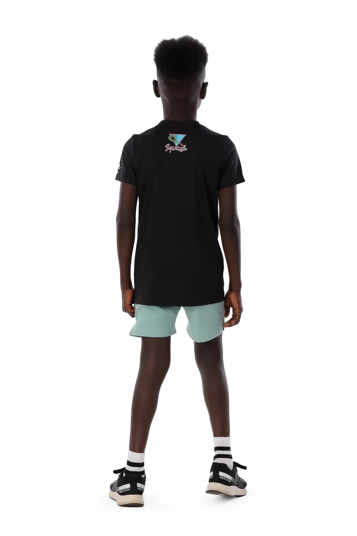 Person wearing a black polo shirt with a logo and light green shorts on a white background