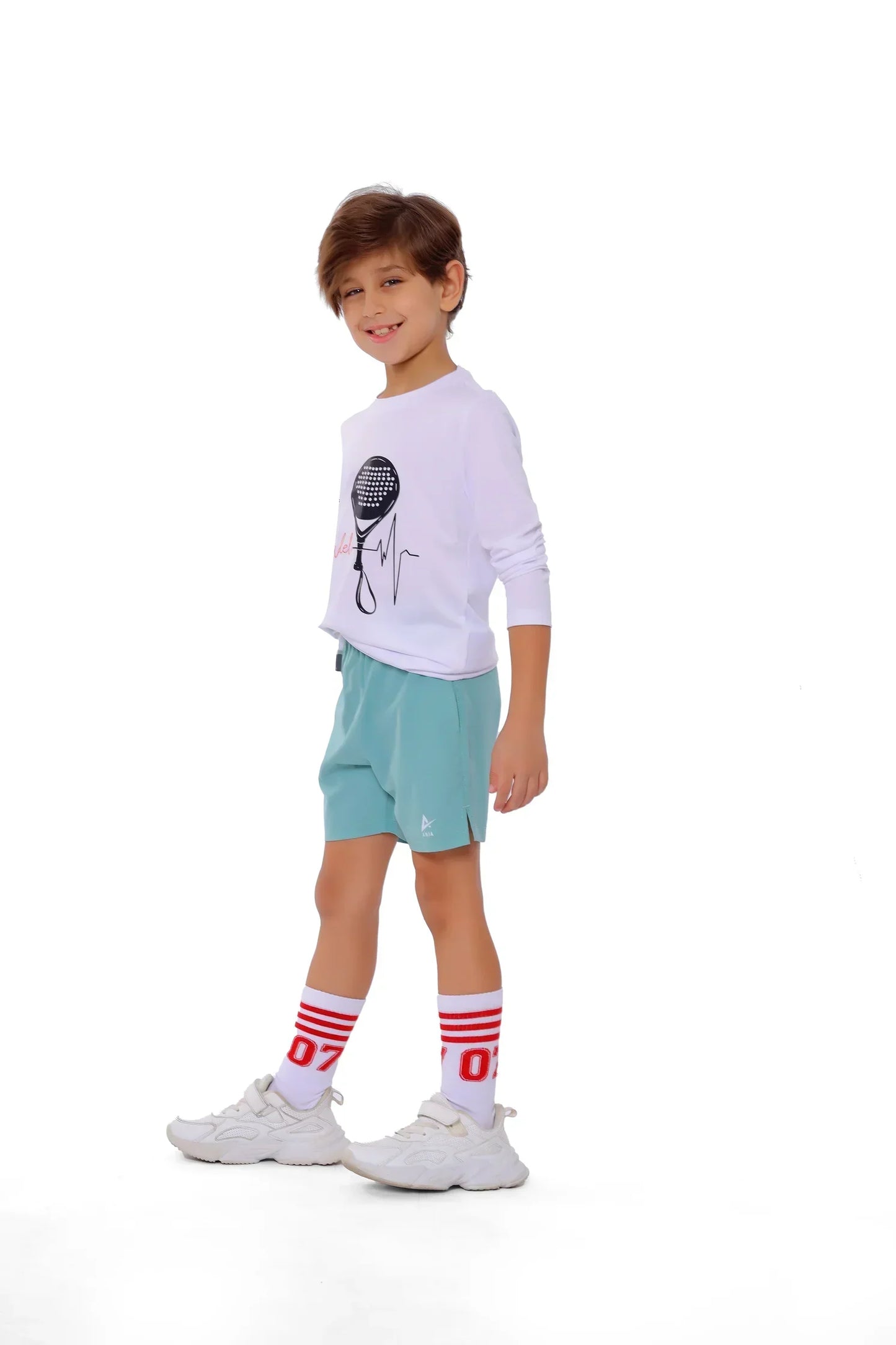 Child wearing a white long-sleeve shirt with a graphic, light blue shorts, and white sneakers on a white background
