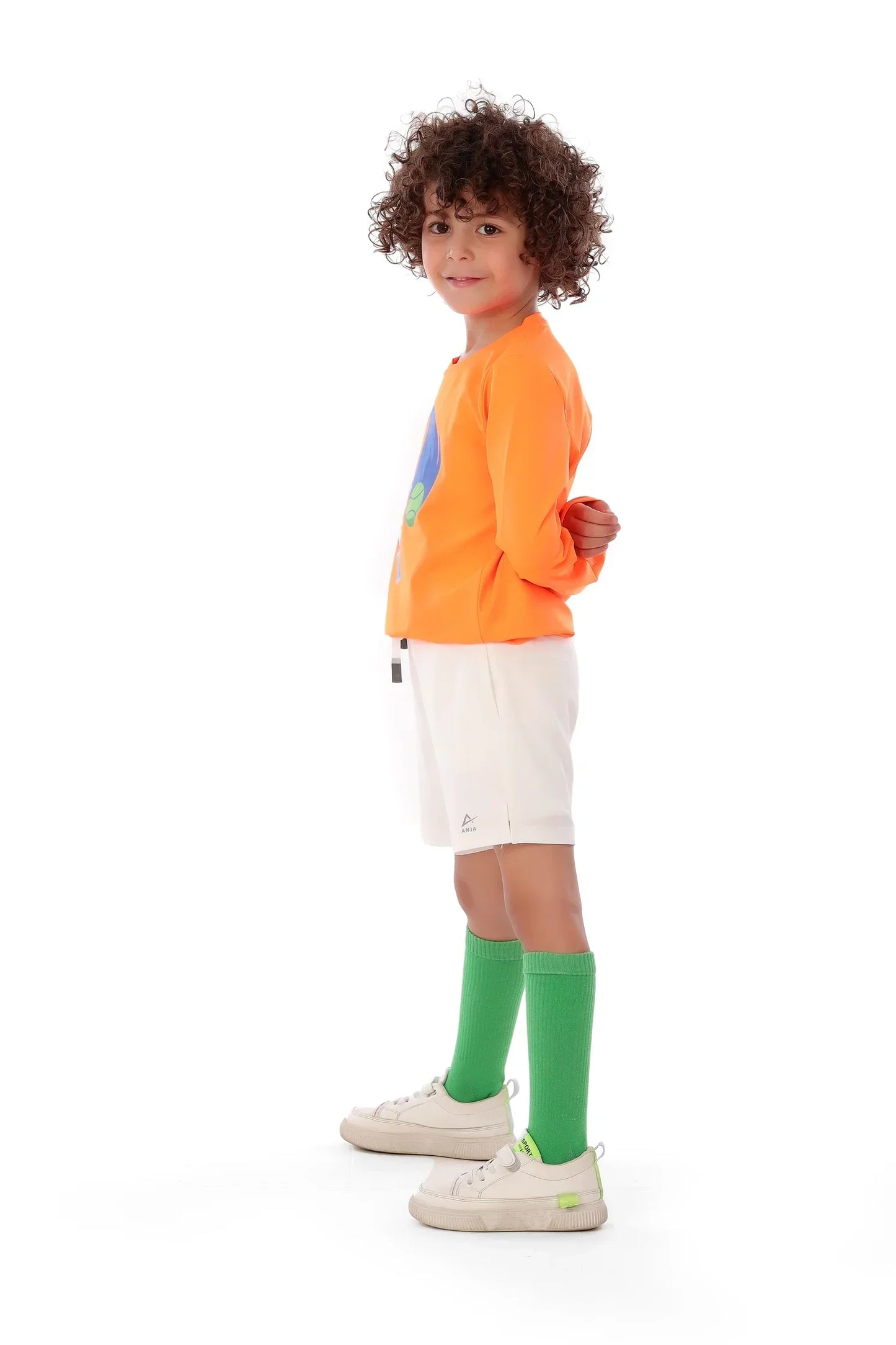 Child wearing an orange sweatshirt, white shorts, and green socks on a white background