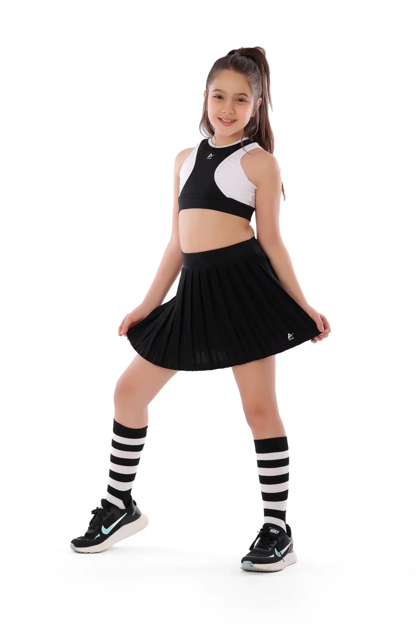 Young girl in a black and white outfit with a pleated skirt on a white background