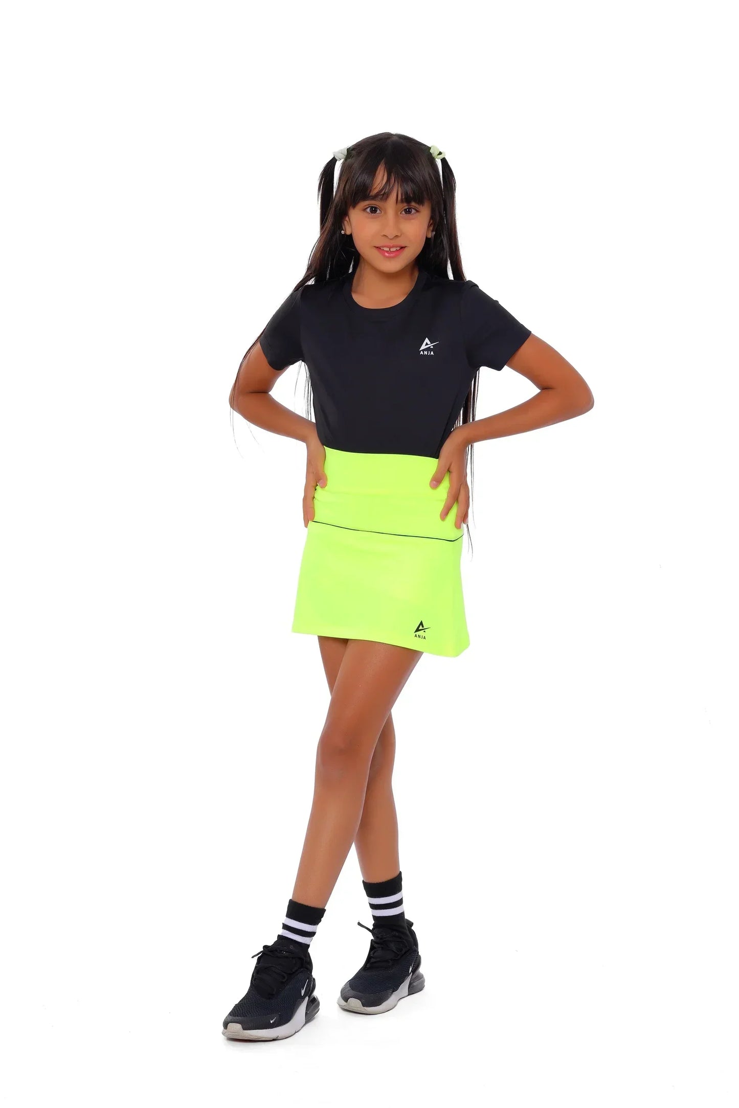 Young girl wearing a black t-shirt and bright green skirt on a white background