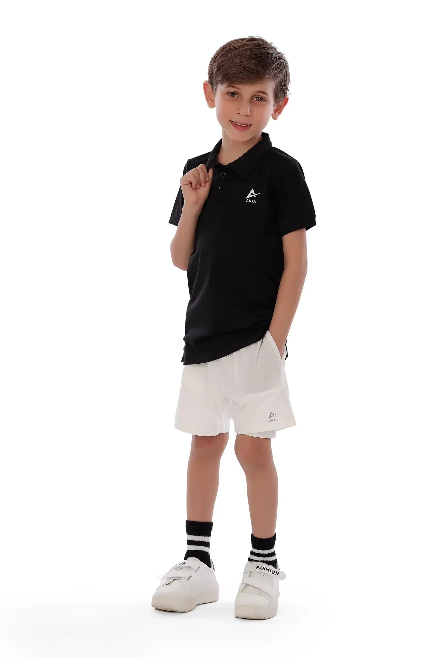 Young boy wearing a black polo shirt and white shorts with a logo on a white background