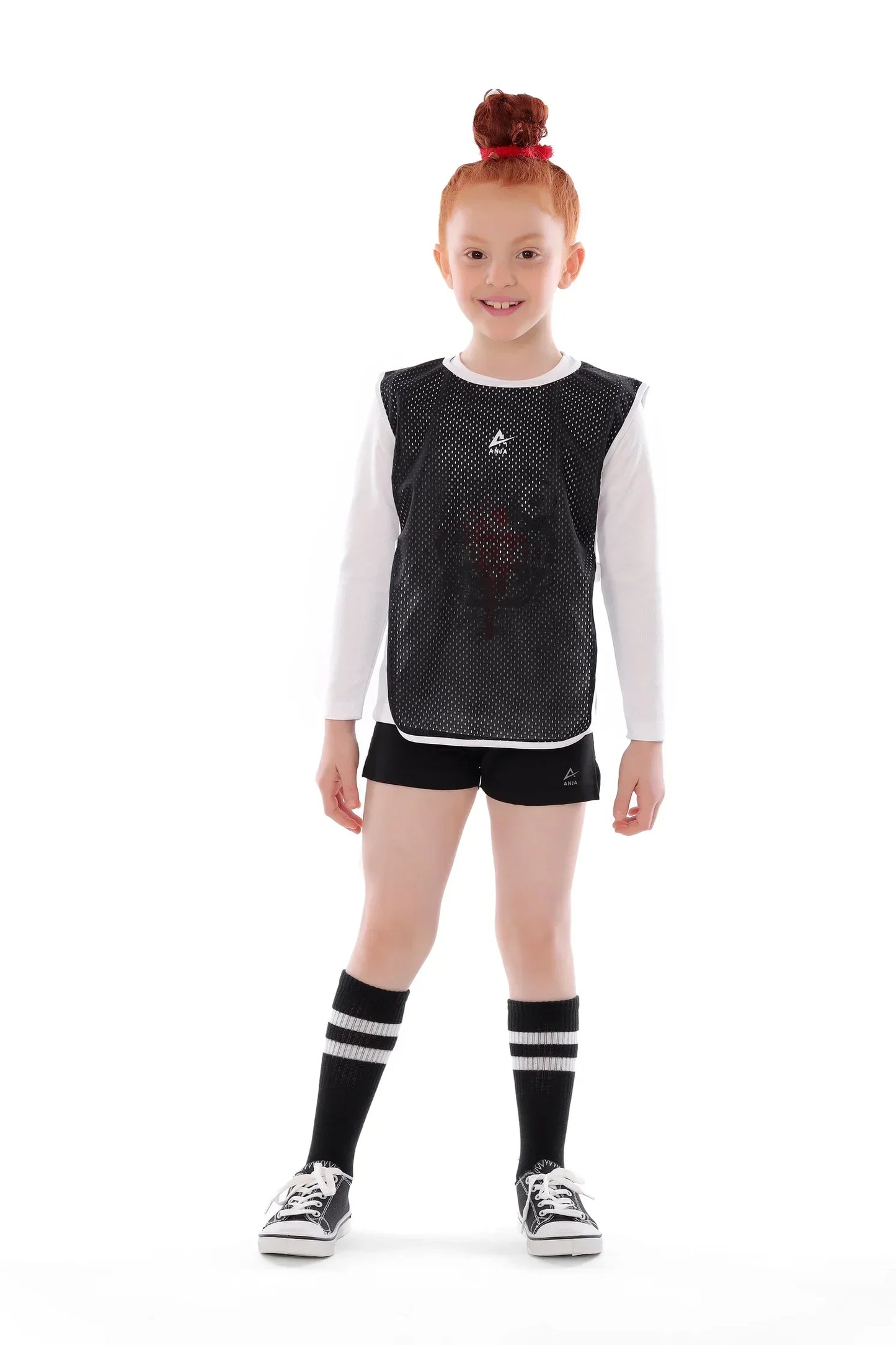 Young girl wearing a black sports jersey, shorts, and socks on a white background