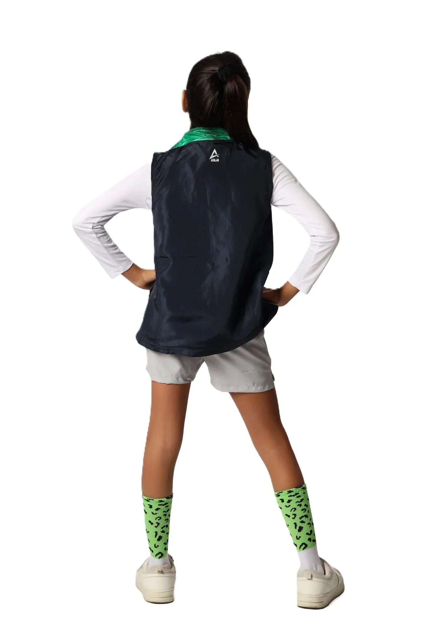 Person wearing a black sleeveless jacket with a logo on the back, white shirt, shorts, and green socks.