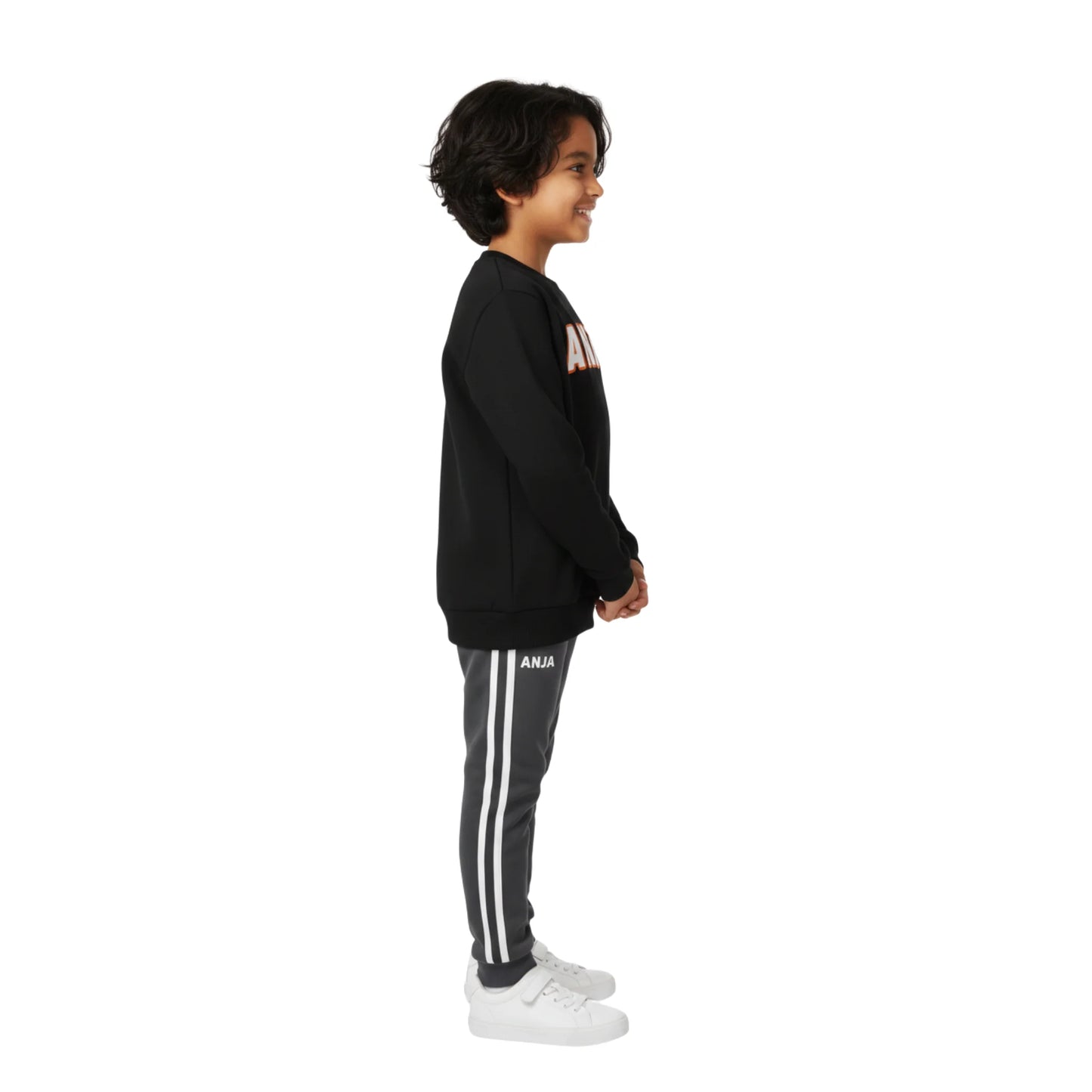 Child wearing a black sweatshirt and gray pants with white stripes on a white background
